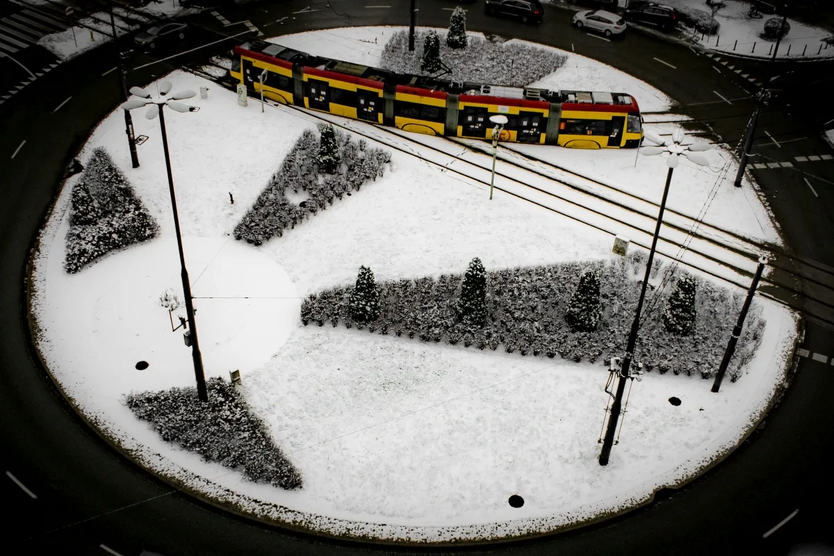 Yellow tram curving around a snow-covered roundabout seen from above